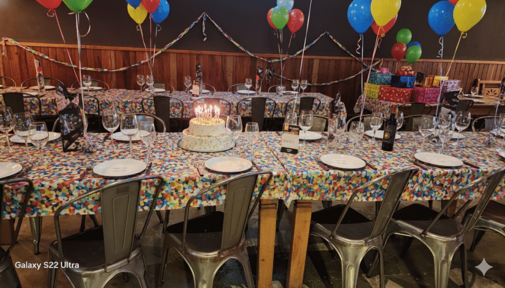 Mesa de festa de aniversário colorida, com bolo de velas acesas, balões e presentes, pronta para um churrasco em Campinas na Ramalho Experience.