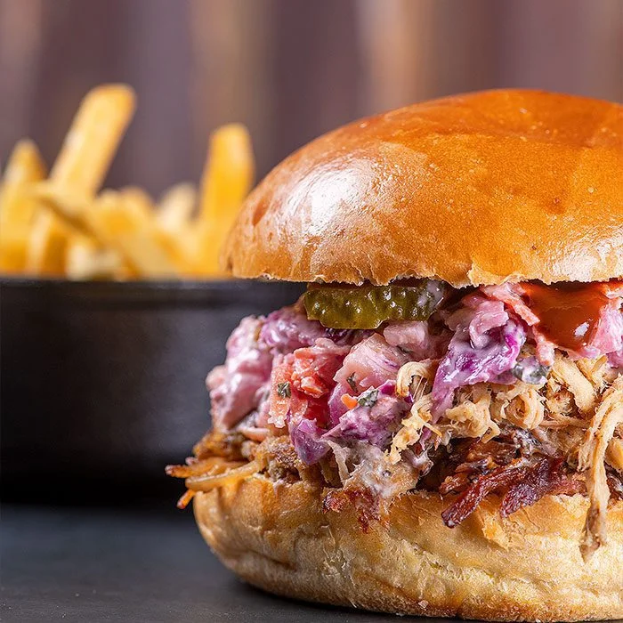 Close-up de um hambúrguer premium em um brioche brilhante e tostado, recheado com carne desfiada suculenta e coleslaw artesanal roxa. Esta é a qualidade do nosso lanche artesanal Campinas.