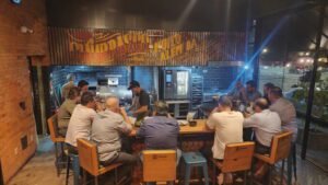 Clientes sentados ao redor do balcão do chef enquanto o churrasqueiro prepara os cortes na grelha, sob o painel Churrasco Muito Além da Churrasqueira, no Ramalho Experience em Campinas